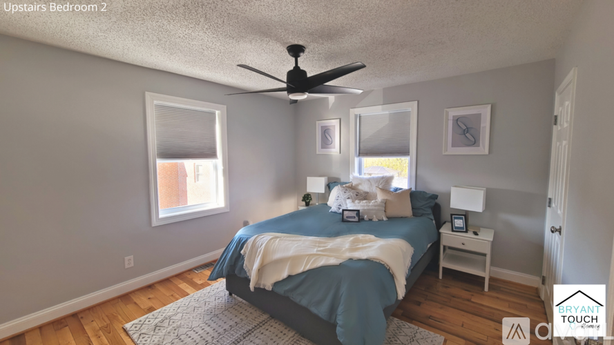 A bedroom with a bed, a ceiling fan, and two windows.