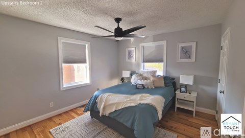 A bedroom with a bed, a ceiling fan, and two windows.