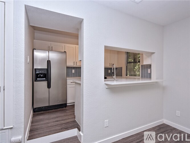 A kitchen with a stainless steel refrigerator and a window with blinds.