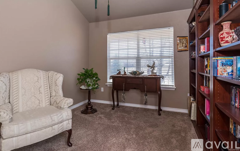 A living room with a white chair, a small table, and a bookshelf filled with books.