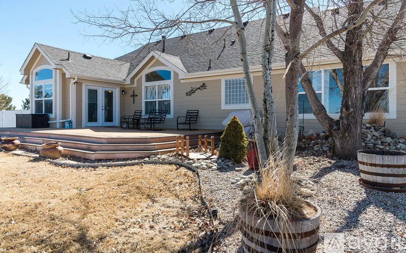 A house with a brown roof and a white fence is surrounded by a gravel area and a few trees.