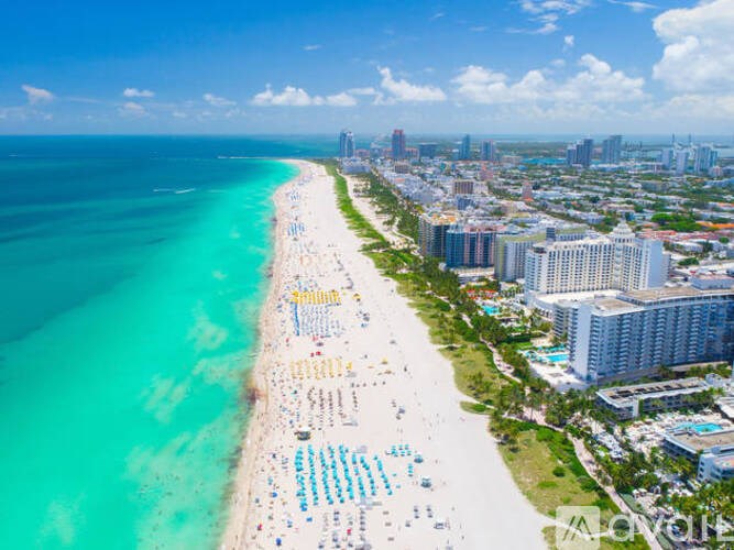 A beach with blue umbrellas and a city skyline in the background.