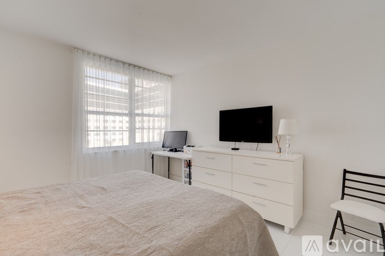 A bedroom with a bed, a television, a chair, and a window with blinds.
