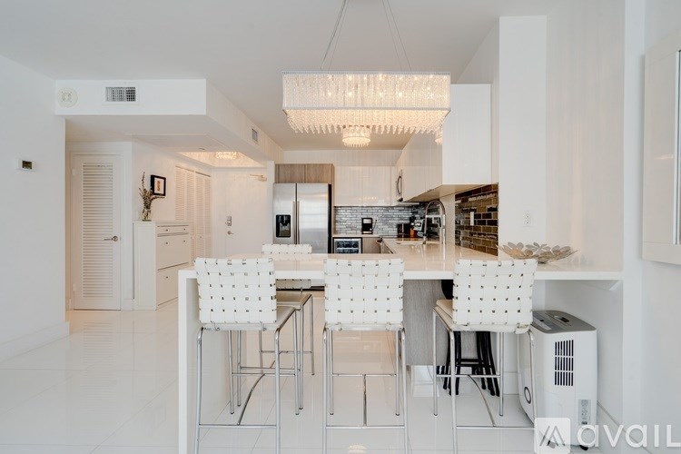 A modern kitchen with white chairs and a glass table.