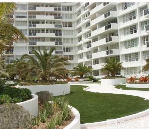 A white building with balconies and a garden in front.