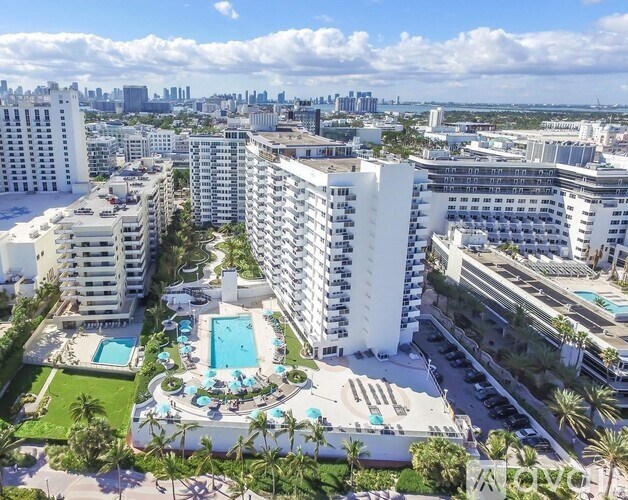A view of a city from a high vantage point with buildings, a pool, and palm trees.