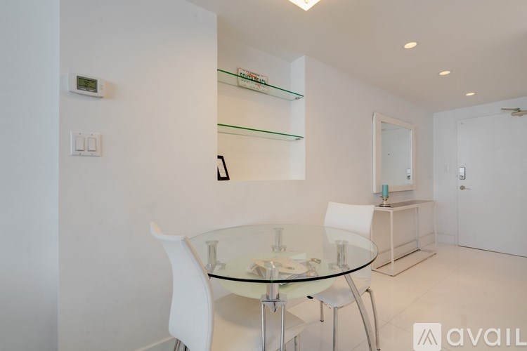 A glass dining table with four white chairs in a white room.