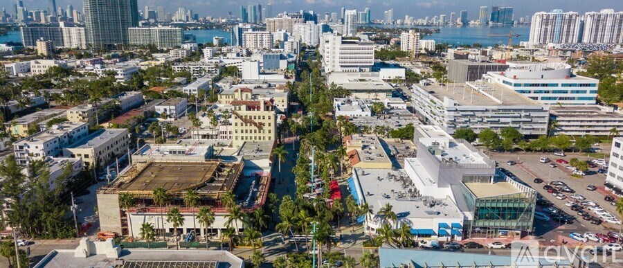 A cityscape with a mix of modern and older buildings, a large open space in the center, and a body of water in the distance.