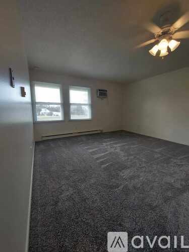 A room with a ceiling fan and two windows.