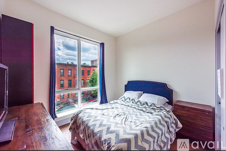 A bedroom with a bed, nightstand, and window overlooking a red brick building.
