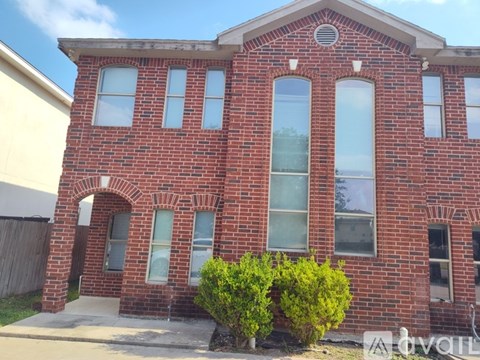 A red brick house with a white window and a bush in front.