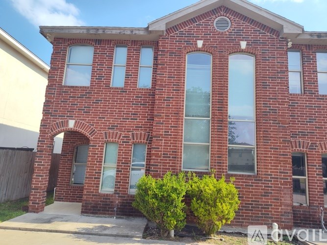 A red brick house with a white window and a bush in front.