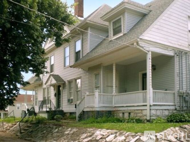 A two-story house with a porch and a stone wall in front.