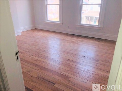 A room with wooden flooring and two windows.