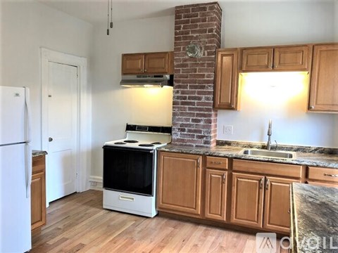 A kitchen with a white fridge, wooden cabinets, and a brick chimney.