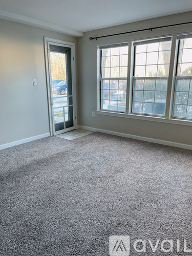 A room with a grey carpet and a window with a view of a parking lot.