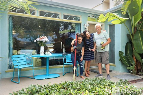 A man, woman and child stand in front of a blue house.