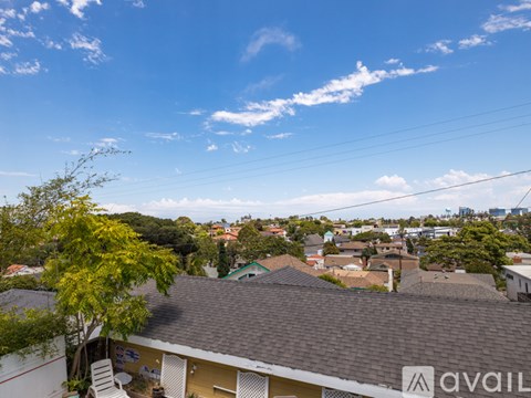A house with a brown roof is surrounded by other houses and trees under a blue sky.