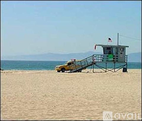 A lifeguard tower sits on a sandy beach with a yellow car parked in front.