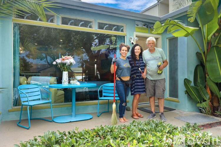 Three people stand in front of a blue house.