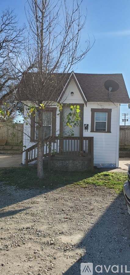 A small white house with a brown roof and a tree in front.