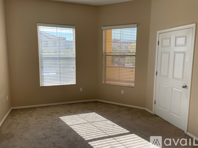 A room with a carpeted floor, a white door, and two windows with blinds.