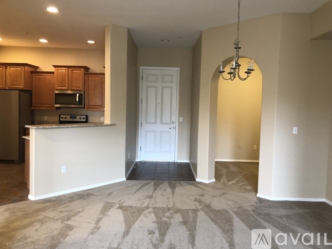 A spacious living room with a kitchen area and a chandelier hanging from the ceiling.