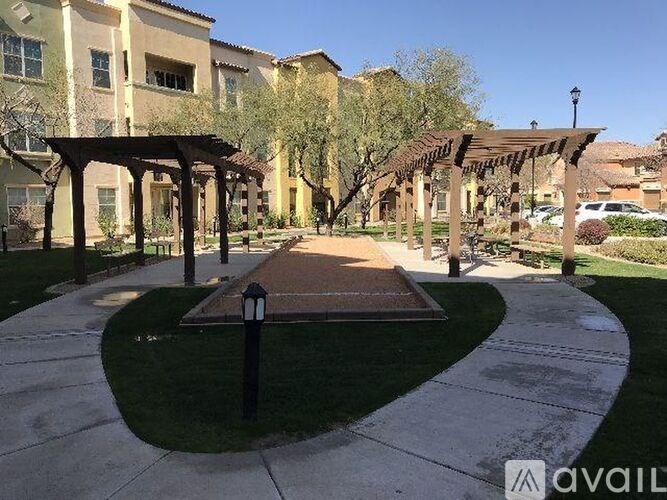 A walkway with a black pole and a pergola in the middle of a grassy area.