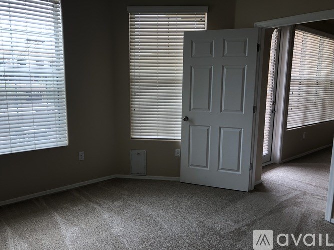 A room with a white door, carpeted floor, and two windows with blinds.