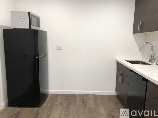 A black refrigerator with a microwave on top sits in a kitchen with wooden floors and white walls.