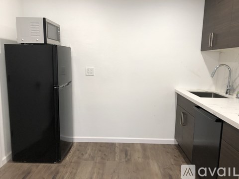 A black refrigerator with a microwave on top sits in a kitchen with wooden floors and white walls.
