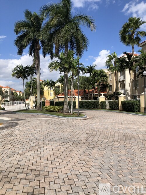 A paved courtyard with palm trees and a white fence.