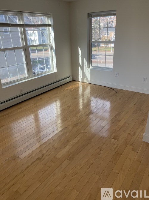 A room with wooden flooring and two windows letting in light.