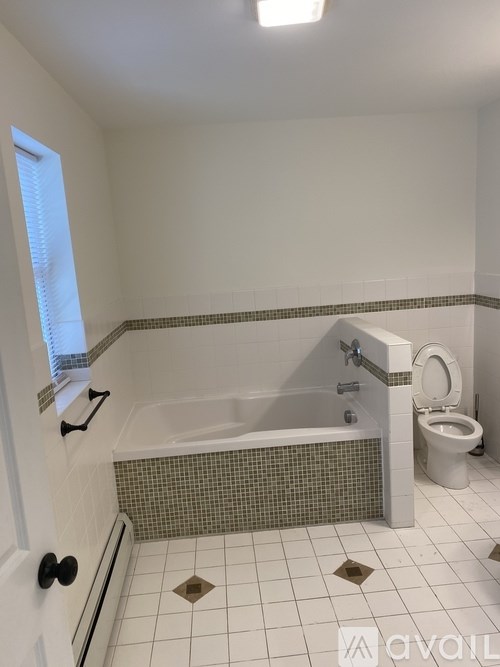 A bathroom with a white toilet and a bathtub with a black handle.