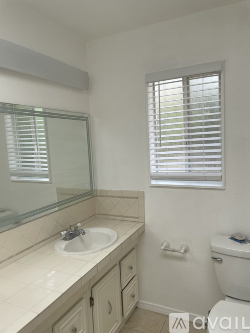 A bathroom with a sink, toilet, and window with blinds.