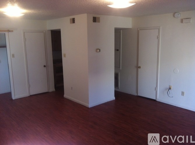A room with wood floors and white walls with four doors.
