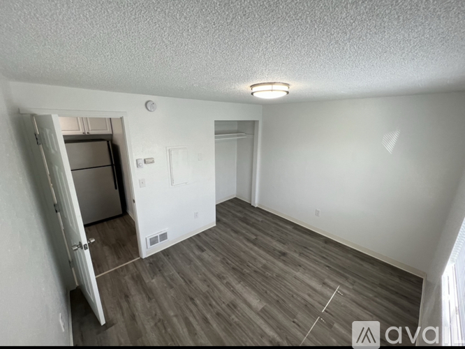 A room with a wooden floor and a white wall with a door and a small window.