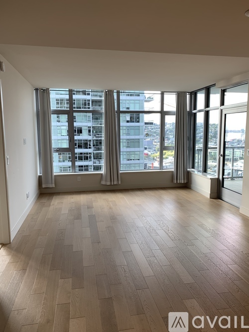 A spacious room with wooden flooring and large windows overlooking a cityscape.