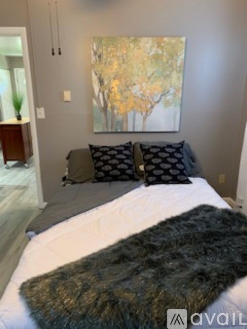 A bedroom with a large painting of trees on the wall above a bed with a black furry throw.