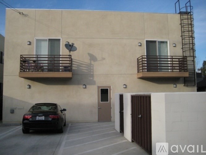 A black car is parked in front of a tan building with a balcony.