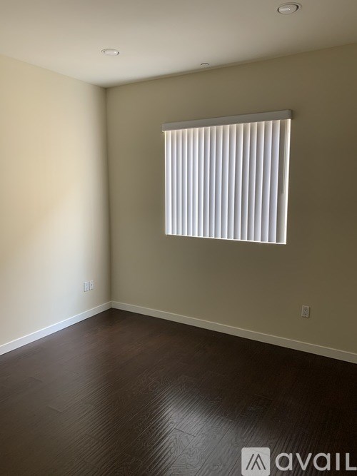 A room with a window covered by white blinds and wooden flooring.