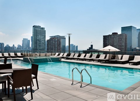 A pool area with chairs and a city skyline in the background.