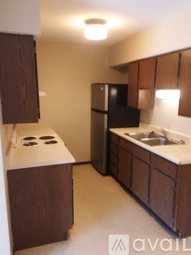 A kitchen with a black fridge and brown cabinets.