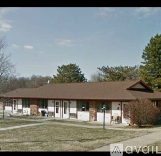 A house with a brown roof and white walls is surrounded by a grassy area and trees.