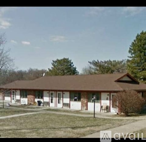 A house with a brown roof and white walls is surrounded by a grassy area and trees.