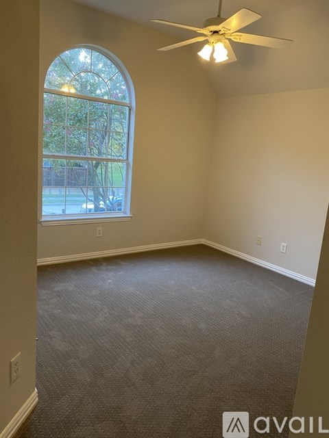 A room with a ceiling fan and a window with a view of trees and a building outside.