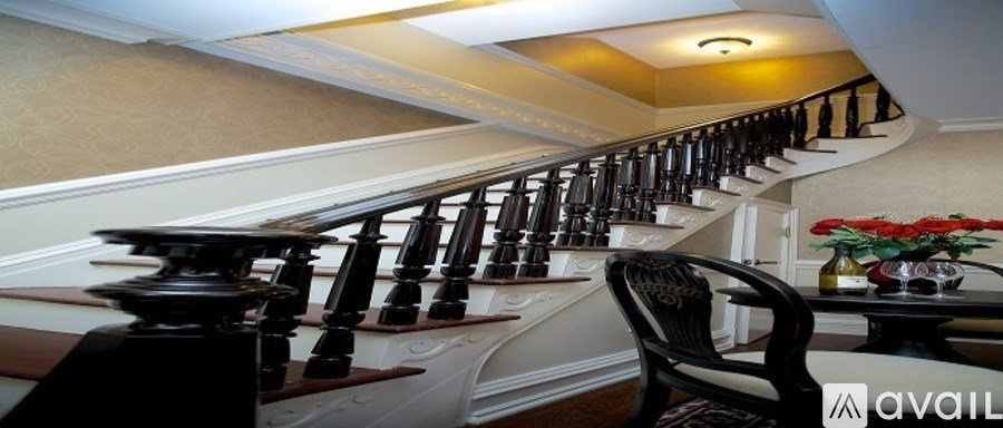 A staircase with a wooden banister and a black chair with a floral arrangement on the table.