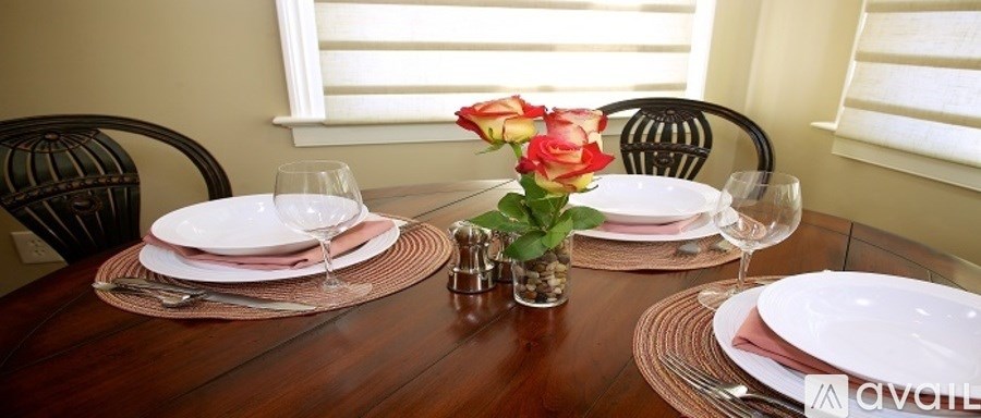 A dining table set with plates, glasses, and a vase of roses.