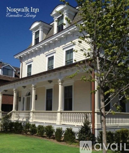 A white house with a balcony and a tree in front of it.