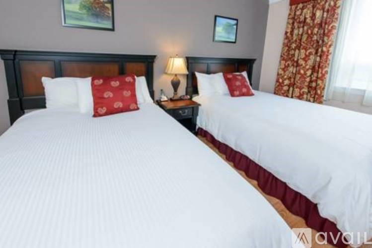 Two beds with white bedspreads and red pillows in a room.